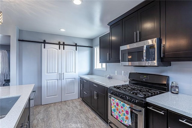 kitchen with dark cabinetry, light stone countertops, a sink, stainless steel appliances, and a barn door