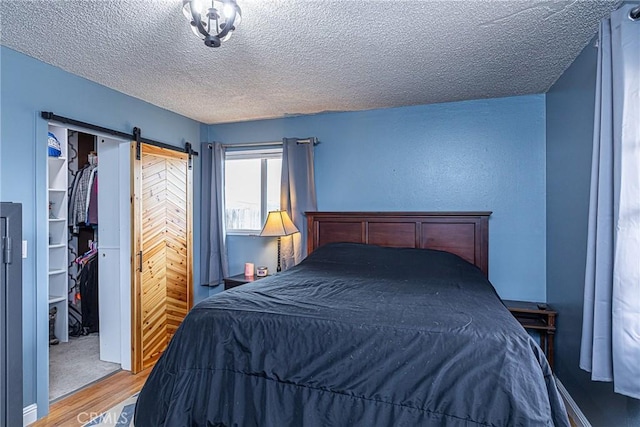 bedroom with wood finished floors, a closet, a textured ceiling, a walk in closet, and a barn door