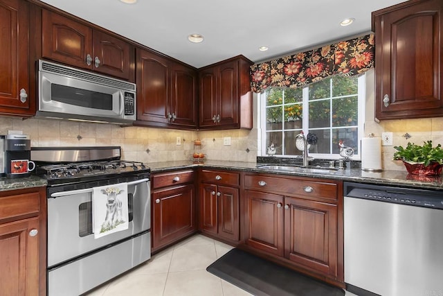 kitchen with dark stone countertops, light tile patterned floors, a sink, appliances with stainless steel finishes, and backsplash