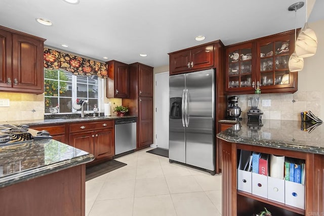 kitchen with a sink, stainless steel appliances, light tile patterned floors, and dark stone counters