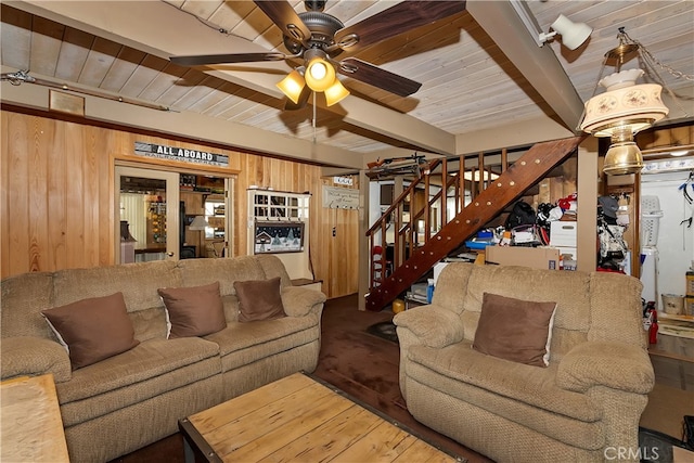 living area with ceiling fan, beamed ceiling, wood walls, stairway, and wood ceiling