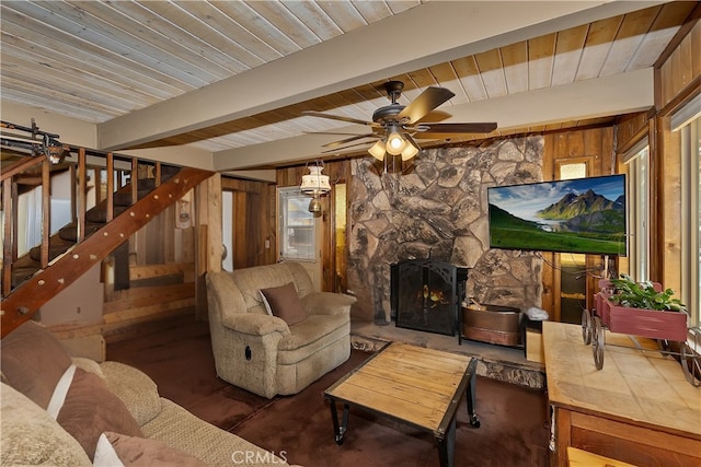 living area with ceiling fan, wood walls, stairs, beam ceiling, and a fireplace