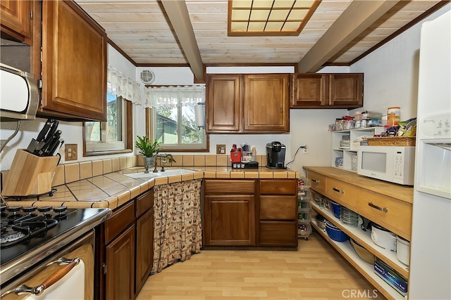 kitchen with white microwave, beam ceiling, tile countertops, and a sink