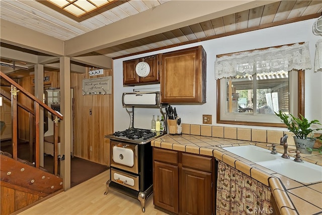 kitchen with range with gas stovetop, tile countertops, brown cabinetry, wooden ceiling, and light wood-type flooring