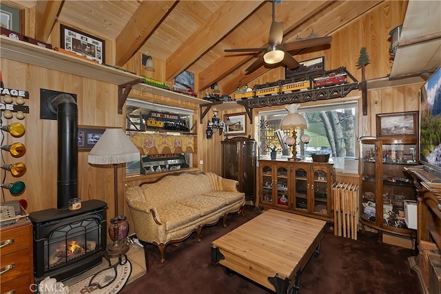 sitting room with a wood stove, wooden walls, wood ceiling, ceiling fan, and vaulted ceiling with beams