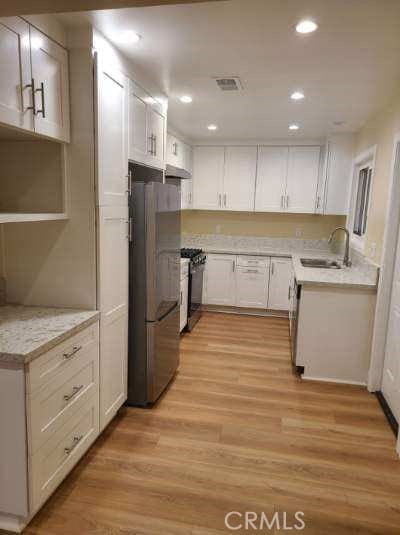 kitchen featuring light wood-type flooring, a sink, gas range oven, freestanding refrigerator, and light countertops