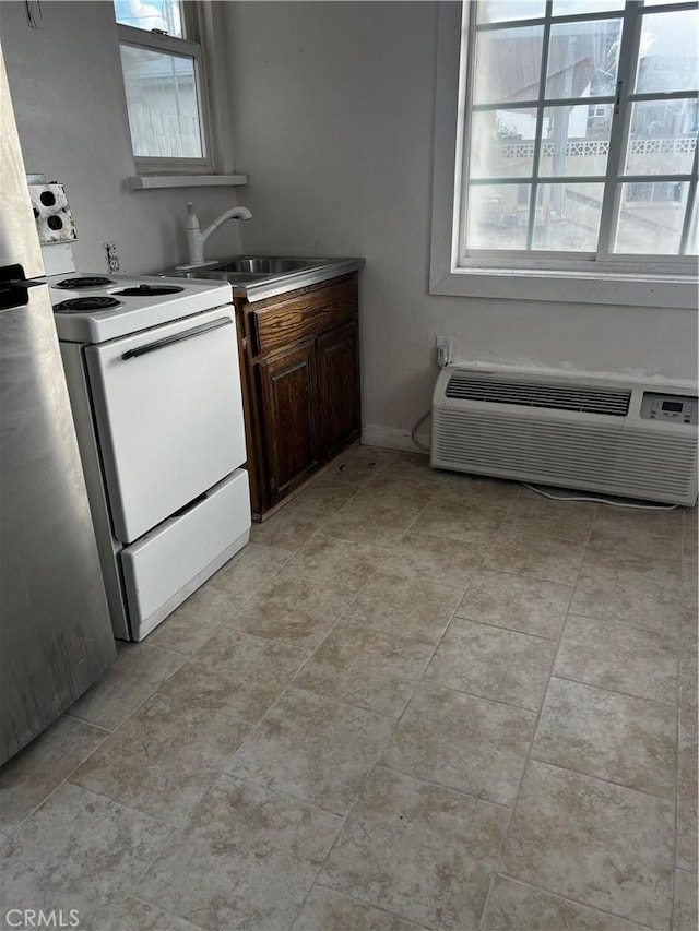 kitchen with a wall unit AC, electric stove, baseboards, and a sink