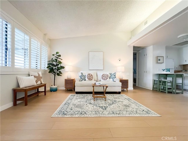 living room with visible vents, a textured ceiling, baseboards, and wood finished floors