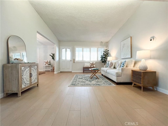 living room with a textured ceiling, light wood-type flooring, baseboards, and vaulted ceiling