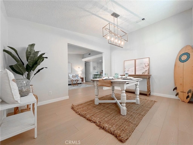 dining room with visible vents, a textured ceiling, an inviting chandelier, and wood finished floors