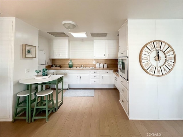 kitchen with visible vents, wood finished floors, white appliances, white cabinetry, and a sink