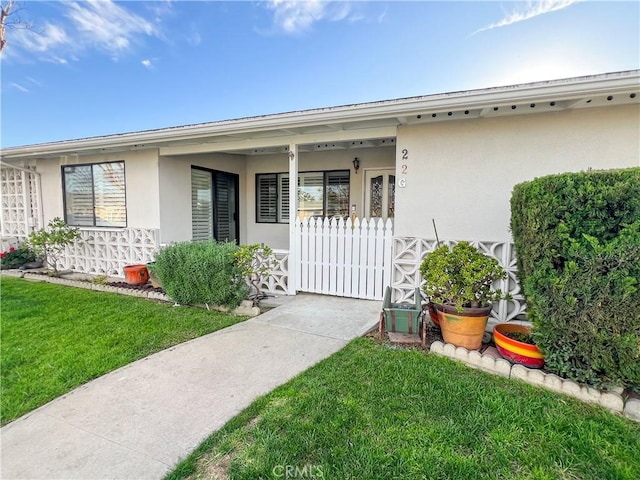 doorway to property with stucco siding, a yard, and covered porch