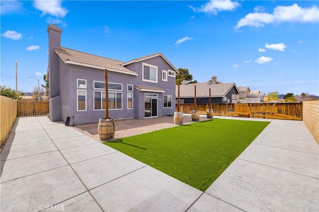 rear view of property with a fenced backyard, stucco siding, a tile roof, a patio area, and a lawn