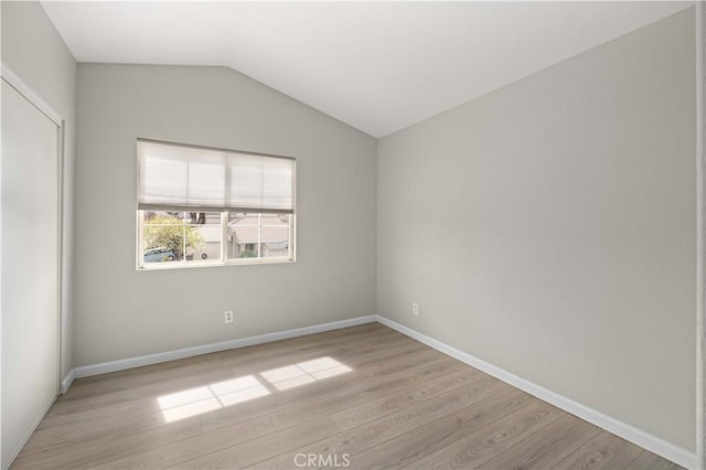 spare room featuring baseboards, light wood-style floors, and vaulted ceiling