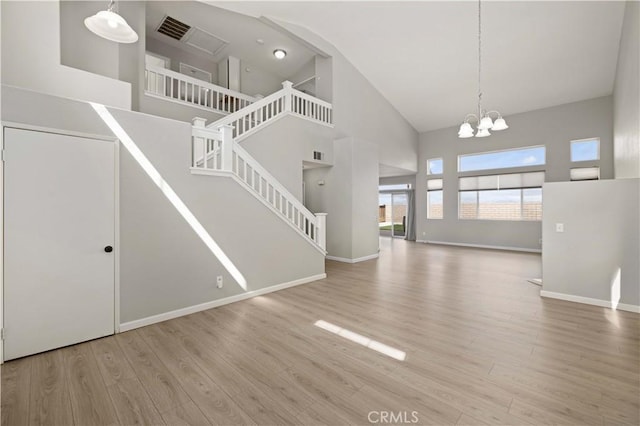 unfurnished living room with visible vents, high vaulted ceiling, a notable chandelier, wood finished floors, and baseboards