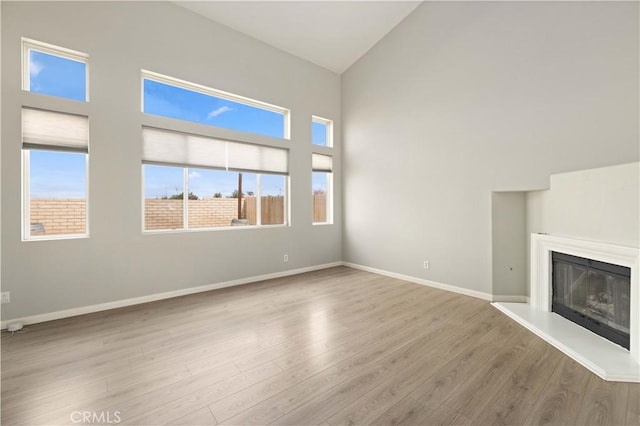 unfurnished living room with a glass covered fireplace, baseboards, high vaulted ceiling, and wood finished floors