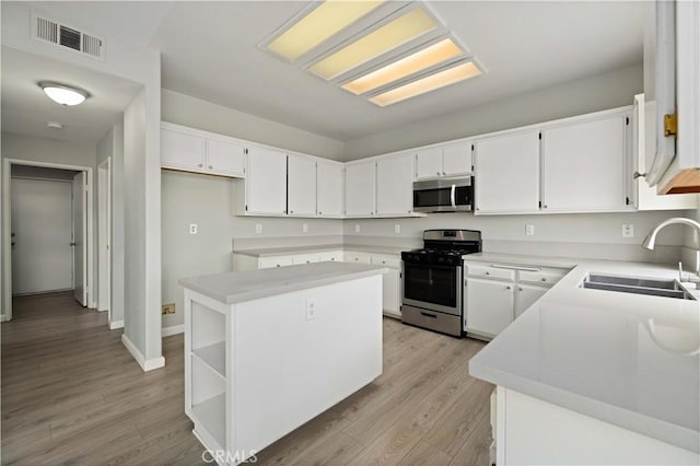 kitchen with light wood finished floors, visible vents, a kitchen island, stainless steel appliances, and a sink