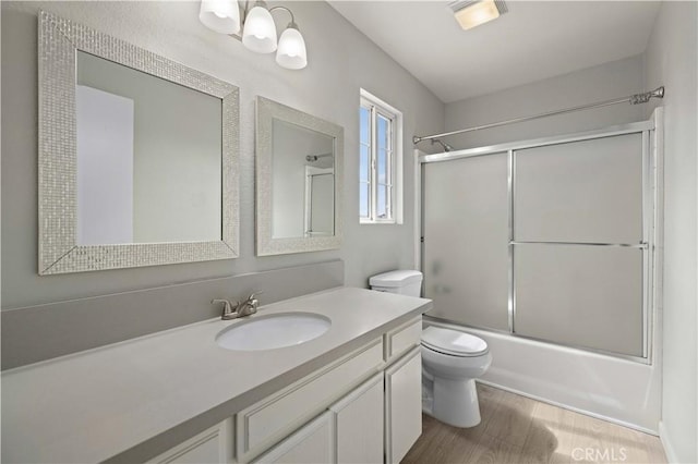 full bath with vanity, toilet, wood finished floors, and bath / shower combo with glass door