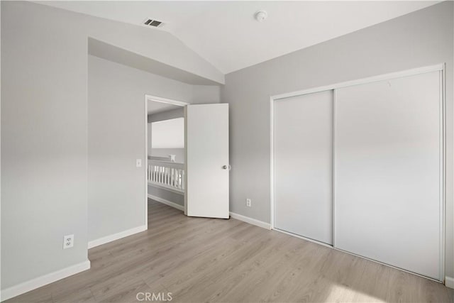 unfurnished bedroom with visible vents, lofted ceiling, wood finished floors, a closet, and baseboards