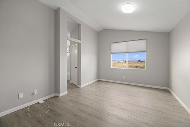 spare room featuring baseboards, lofted ceiling, and wood finished floors