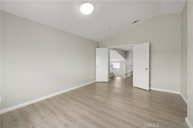 spare room featuring visible vents, light wood finished floors, baseboards, and vaulted ceiling