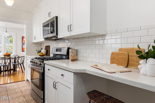 kitchen with light tile patterned floors, light stone countertops, stainless steel appliances, white cabinetry, and tasteful backsplash