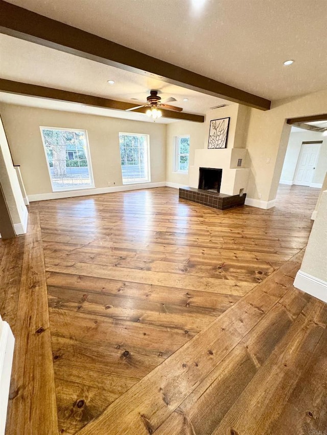 unfurnished living room with beam ceiling, a wealth of natural light, a fireplace with raised hearth, and wood-type flooring