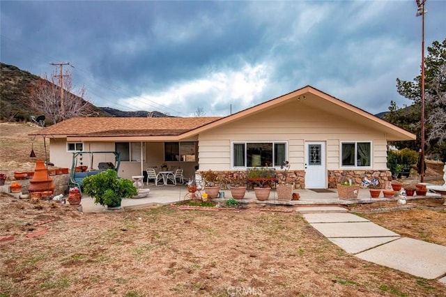 rear view of house with stone siding and a patio area