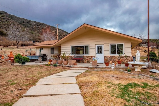 back of property with a mountain view, a patio area, stone siding, and a lawn