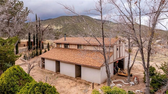 view of side of home featuring stucco siding, a garage, a mountain view, and a shingled roof