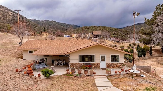 rear view of house featuring a patio area, stone siding, and a mountain view