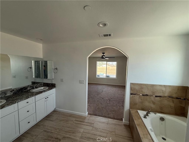 full bathroom with baseboards, double vanity, a sink, a relaxing tiled tub, and visible vents