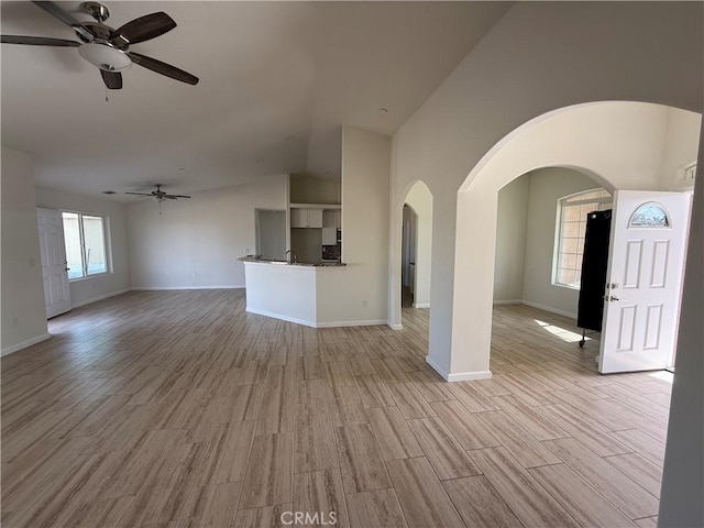 unfurnished living room featuring ceiling fan, light wood finished floors, vaulted ceiling, and baseboards
