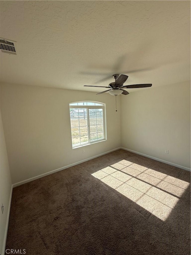 empty room featuring visible vents, dark colored carpet, and baseboards