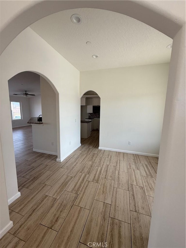 spare room with ceiling fan, light wood-type flooring, arched walkways, and baseboards