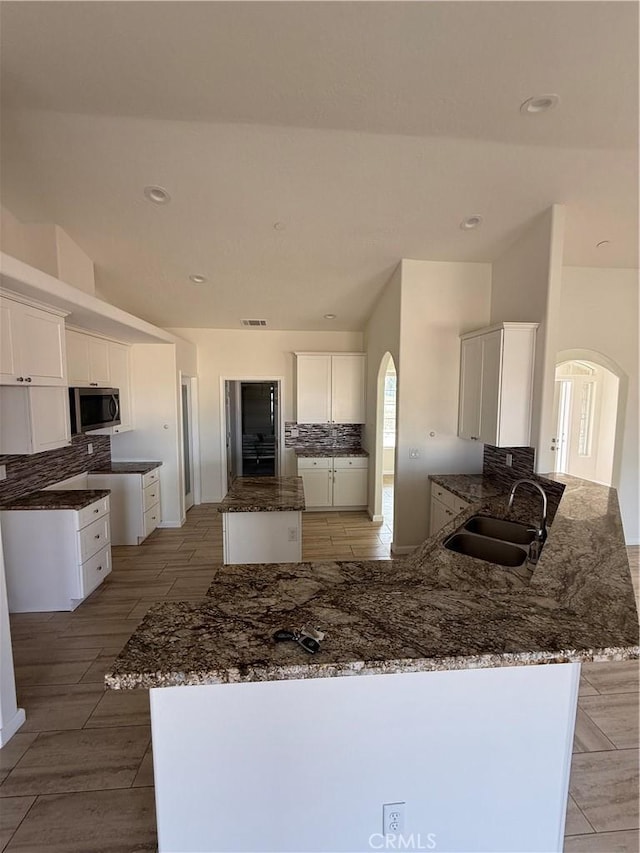 kitchen featuring stainless steel microwave, a peninsula, arched walkways, and a sink
