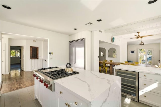 kitchen featuring light stone countertops, light tile patterned flooring, stainless steel appliances, wine cooler, and white cabinets