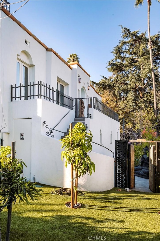 view of side of home featuring stucco siding, a lawn, a balcony, and a tiled roof