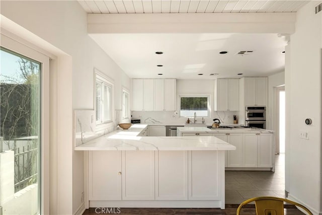 kitchen featuring visible vents, a sink, a peninsula, appliances with stainless steel finishes, and decorative backsplash