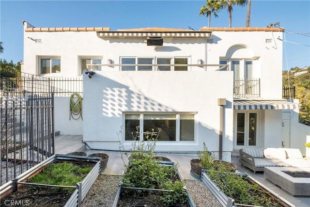 rear view of house featuring a balcony, french doors, fence, and stucco siding