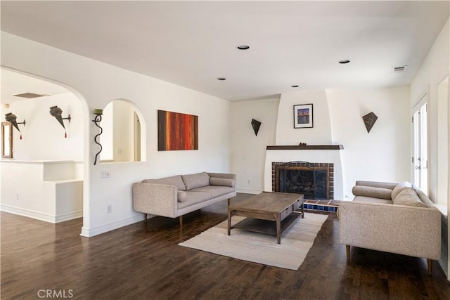 living room featuring visible vents, a brick fireplace, baseboards, and wood finished floors