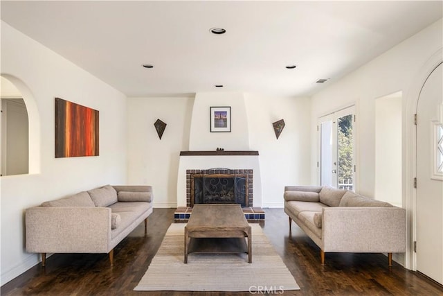 living room featuring dark wood-style floors, visible vents, a fireplace with raised hearth, and baseboards