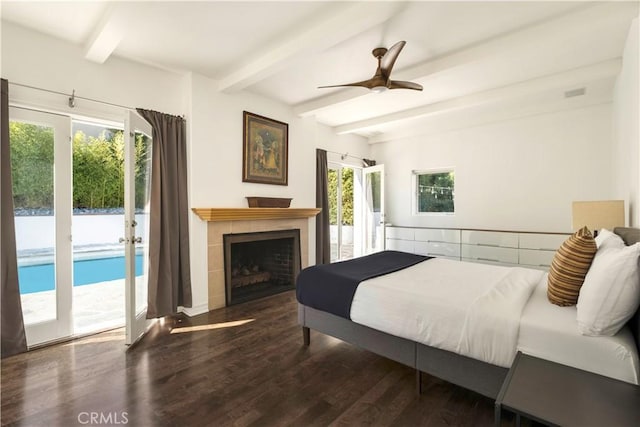 bedroom with beamed ceiling, a ceiling fan, a tiled fireplace, access to outside, and wood finished floors