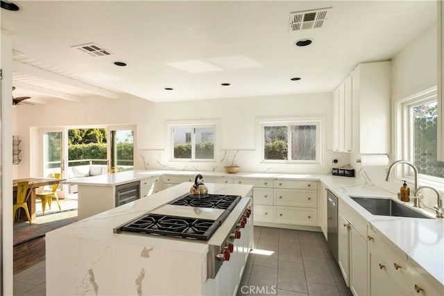 kitchen featuring light stone counters, visible vents, a sink, wine cooler, and a center island