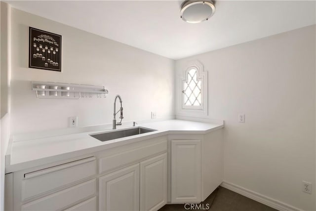 kitchen featuring white cabinets, light countertops, baseboards, and a sink