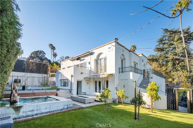 back of house featuring a balcony, fence, stucco siding, stairs, and a lawn