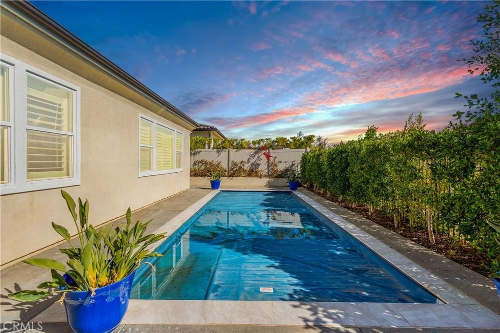 pool at dusk featuring a fenced in pool and a fenced backyard