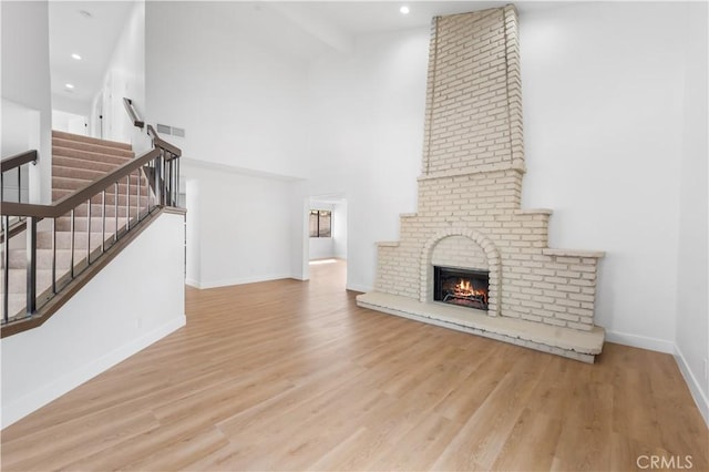 unfurnished living room with visible vents, baseboards, stairs, a high ceiling, and wood finished floors