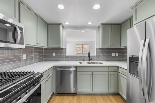 kitchen with light stone countertops, a sink, stainless steel appliances, light wood-type flooring, and backsplash