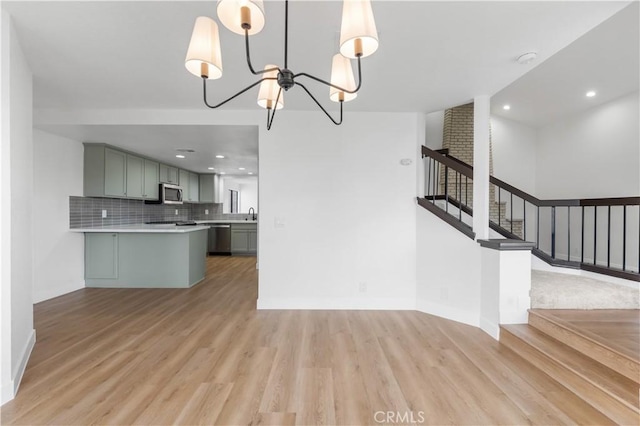 kitchen with a notable chandelier, stainless steel appliances, light wood finished floors, decorative backsplash, and light countertops